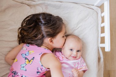 Küçük kız bir yatakta küçük kız kardeşine sarılıp onu öpüyor.