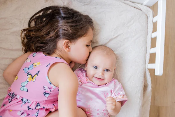 Klein meisje liefdevol knuffelen en kussen haar gelukkig zusje op een bed — Stockfoto