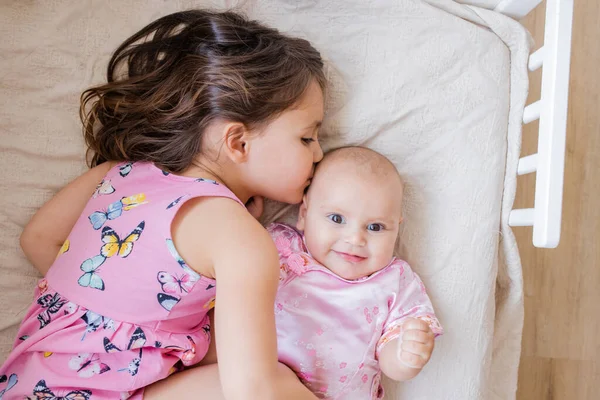 Klein meisje liefdevol knuffelen en kussen haar gelukkig zusje op een bed — Stockfoto