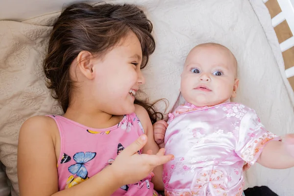 Gelukkig klein meisje liggend op een bed met haar zusje en glimlachen naar haar — Stockfoto