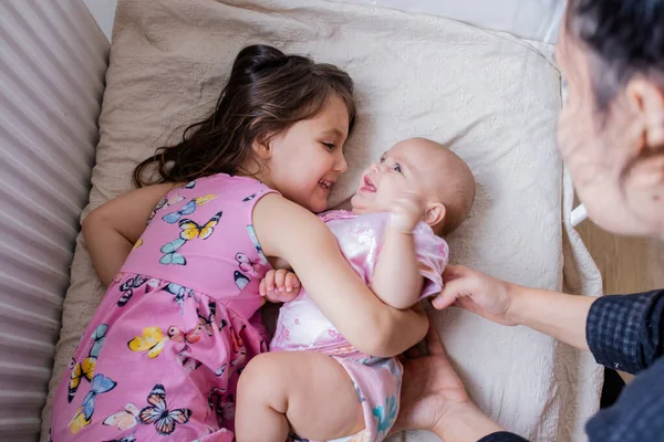 Joyful little girl smiling and hugging her happy baby sister on a bed