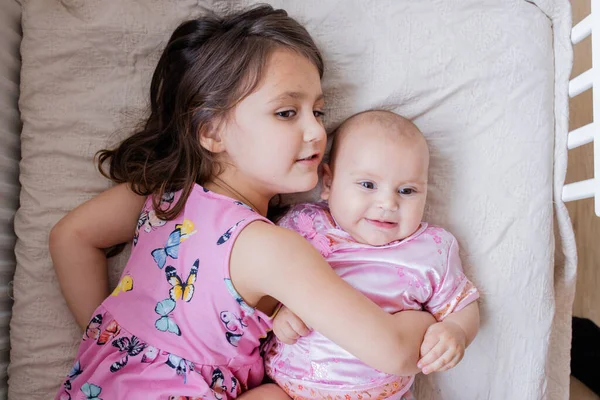 Happy little girl lying down on a bed and hugging her baby sister