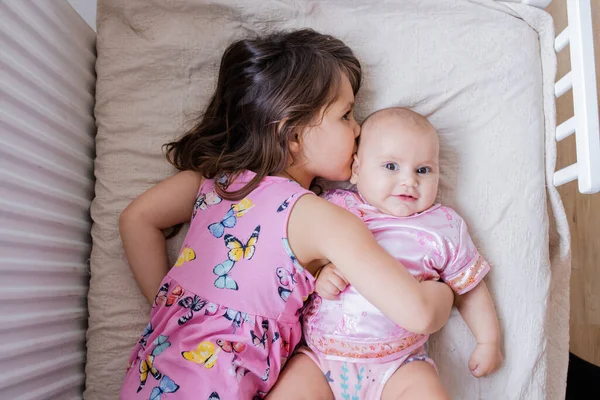 Klein meisje liggend op een bed en vreedzaam knuffelen haar gelukkig zusje — Stockfoto