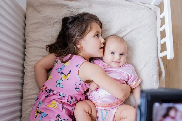 Счастливая маленькая девочка лежит на кровати и обнимает свою младшую сестру — стоковое фото