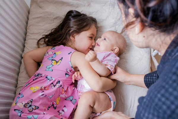 Joyful klein meisje glimlachen en knuffelen haar gelukkig zusje op een bed — Stockfoto