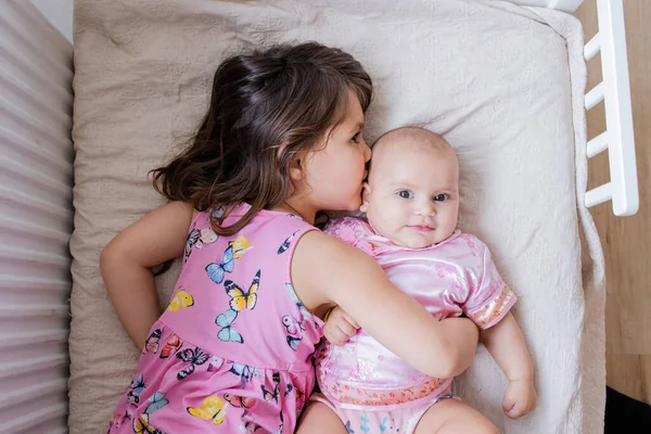 Klein meisje liggend op een bed en vreedzaam knuffelen haar gelukkig zusje — Stockfoto