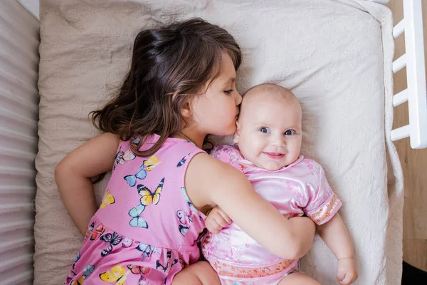 Little girl lovingly hugging and kissing her baby sister on a bed