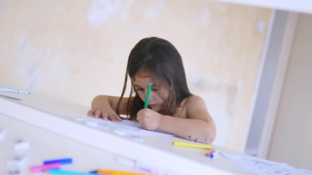 Petite fille réfléchie sur un miroir colorant avec un crayon vert — Video