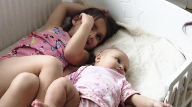 Küçük mutlu kız, pembe elbiseli kız kardeşinin yanına uzandı.