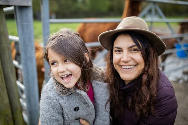 Matka i córka uśmiechnięte do kamery z brązowymi alpakami za nimi — Zdjęcie stockowe