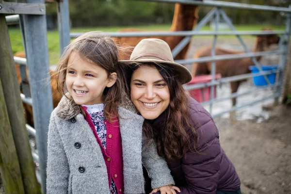 Sorridente madre e figlia guardando la distanza con alpaca dietro di loro — Foto Stock