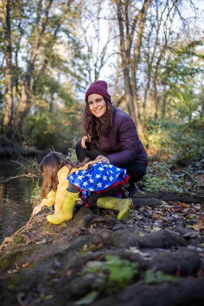 Glückliche Mutter und Tochter spielen neben einem Fluss im Wald — Stockfoto