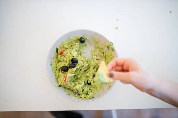 Vrouwelijke hand dompelen nacho 's in guacamole saus met olijven — Stockfoto
