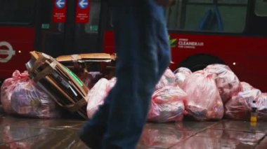 Terk edilmiş karton ve kaldırımda duran pembe plastik çöp torbaları.