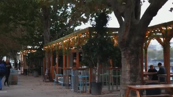 Illuminated wooden pergola above chairs and tables and surrounded by trees — Stock Video