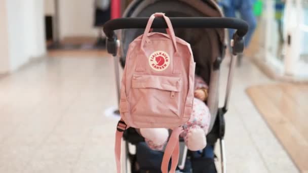 Vrouw duwen een kinderwagen met een roze rugzak opknoping van de handgreep — Stockvideo