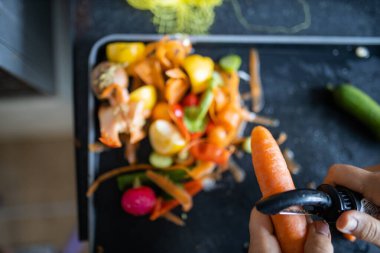 Kadın eli, organik çöplerin üzerinde havuç soyuyordu.