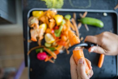 Kadın eli, organik çöplerin üzerinde havuç soyuyordu.