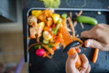 Kadın eli, organik çöplerin üzerinde havuç soyuyordu.