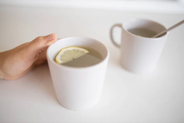 Hand holding a cup of lemon tea with a lemon slice inside