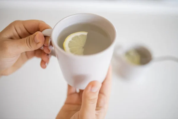 Руки держат чашку лимонного чая с ломтиком лимона внутри — стоковое фото