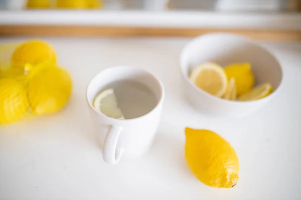 Чашка лимонного чая на белом столе в окружении лимонов — стоковое фото