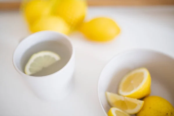 Чашка лимонного чая на белом столе в окружении лимонов — стоковое фото