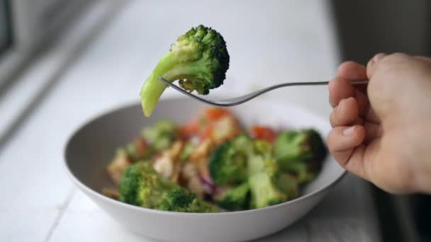 Gaffelplockning av broccoli från broccoli och kycklingsallad bredvid ett fönster — Stockvideo