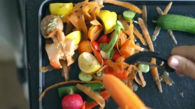 Kadın eli, havucu nazikçe organik çöplerin üzerine soyar.