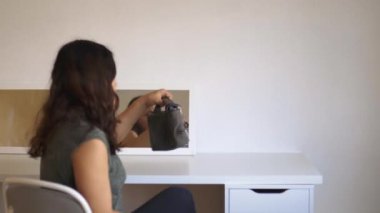 Kadın aynanın önünde oturuyor ve sakince makyaj yapmaya hazırlanıyor.