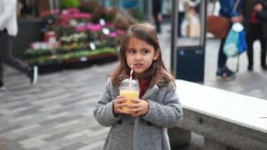 Küçük mutlu kız arkasında insanlar olan sarı bir meyve suyu yudumluyor.