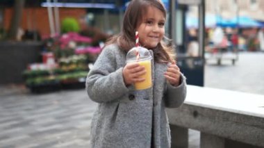 Küçük mutlu kız kaydedilirken sarı bir smoothie yudumluyor