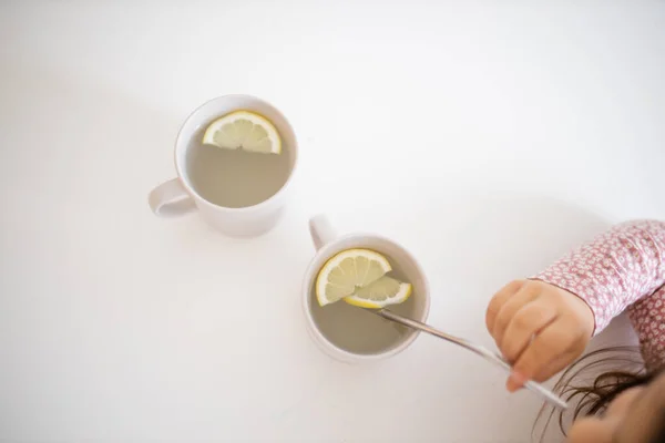 Девочка за столом пьет чашку лимонного чая — стоковое фото