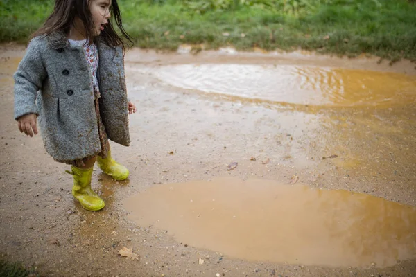 Fröhliches kleines Mädchen hüpft und planscht fröhlich in einer schlammigen Pfütze — Stockfoto