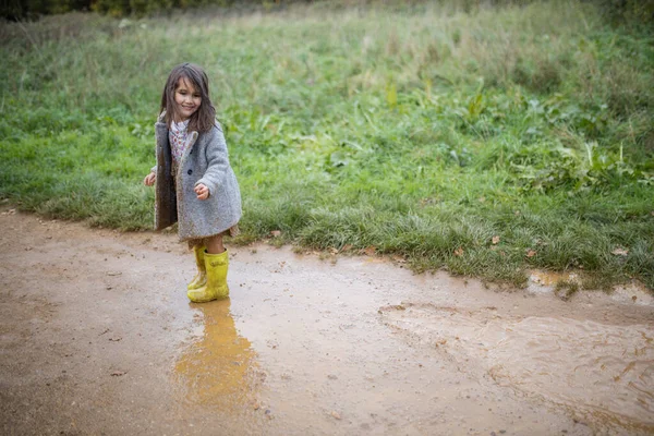 Glückliches kleines Mädchen lächelt nach einem Sprung in eine schlammige Pfütze — Stockfoto