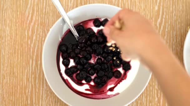 Kvinnlig hand strö granola ovanpå yoghurt och blåbär — Stockvideo