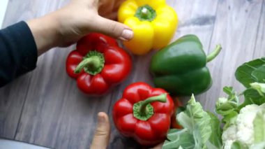 Kadın elleri ahşap bir masada renkli dolma biberleri birleştiriyor.