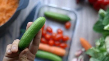 Kadın eli, plastik bir kabın içine sebzeyle salatalık koyuyor.