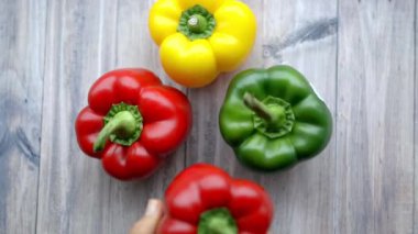 Kadın elleri ahşap bir masada renkli dolma biberleri birleştiriyor.