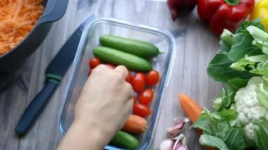 Sebzeli plastik bir kabın içinden domates toplayan bir kadın.