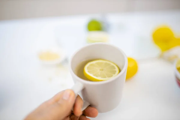 Женщина держит чашку лимонного чая над лаймами и лимонами — стоковое фото