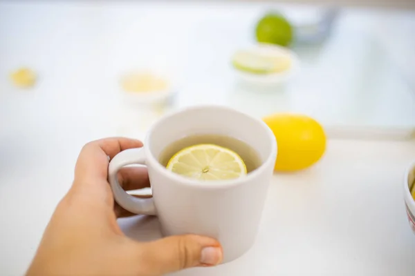 Женщина держит чашку лимонного чая над лаймами и лимонами — стоковое фото