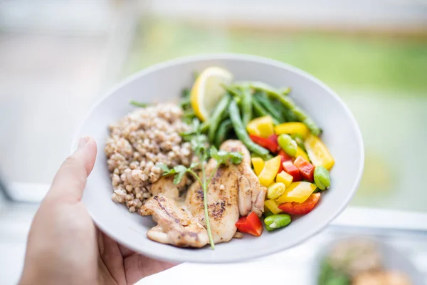Elinde tavuk ve yeşil fasulyeli karabuğday tabağı var.