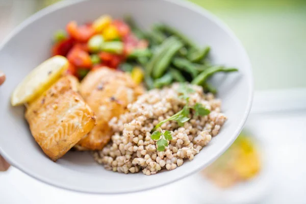 Hand holding salmon and buckwheat dish with green beans