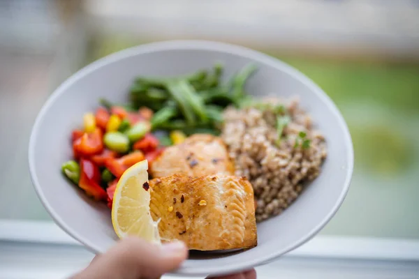 Hand holding salmon and buckwheat dish with green beans