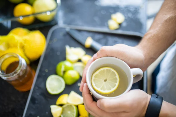 Мужские руки держат чашку лимонного чая над ломтиками лайма — стоковое фото