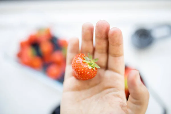 Strawberry on a hand above blurry berries in containers