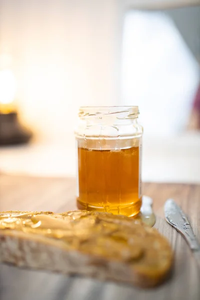 Honey jar and a slice of bread with peanut butter on wooden table — Stock Photo, Image