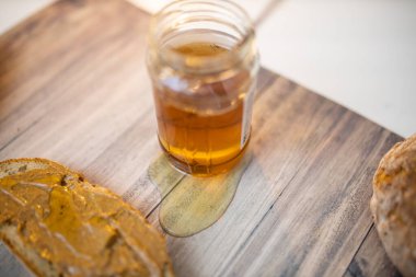 Bal kavanozu ve tahta masada fıstık ezmeli bir dilim ekmek.