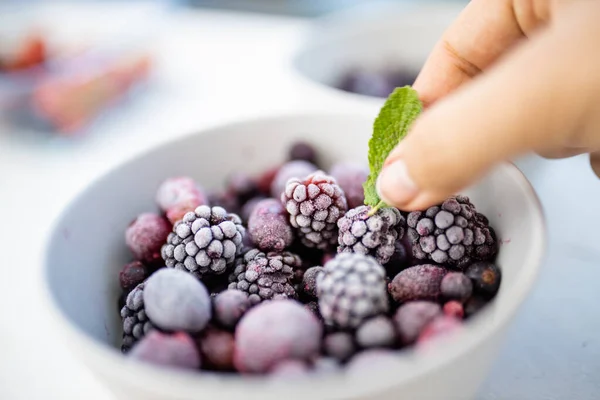 Kvinnlig hand som håller ett mintblad på en skål björnbär — Stockfoto